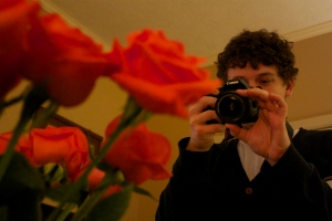 A man taking a picture of a bunch of roses.